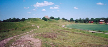 Gamla Uppsala is an area rich in archaeological remains seen from the  field whose larger  (left part) are close to the royal mounds. The building beyond the mounds is the church and to its right is the low -mound and then the museum.
