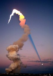 Shuttle Launch at Sunset. The sun is behind the camera, and the shadow of the plume is cast across the roof of the sky, intersecting the moon.