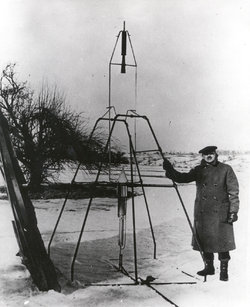 Robert Goddard, bundled against the cold  weather of , , holds the launching frame of his most notable invention — the first liquid-fueled rocket.
