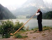 A Swiss playing alphorn near a mountain lake