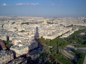 A Parisian view from the second level of the Eiffel Tower, with  creeping at the horizon, barely past the towering shadow.